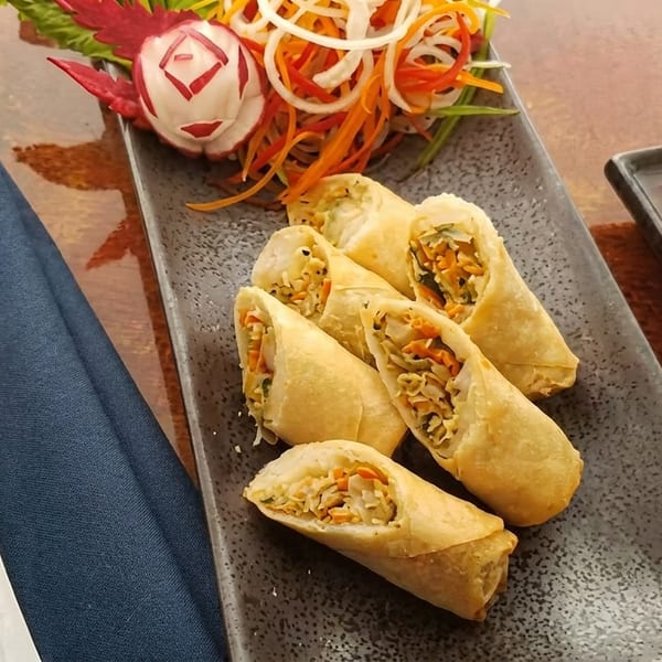 Crispy spring rolls with vegetable filling, dipping sauce, and a decorative salad on a dark plate.