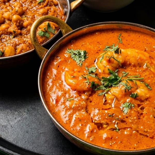 Two brass bowls of Indian food, one with chickpea curry and the other with shrimp curry.