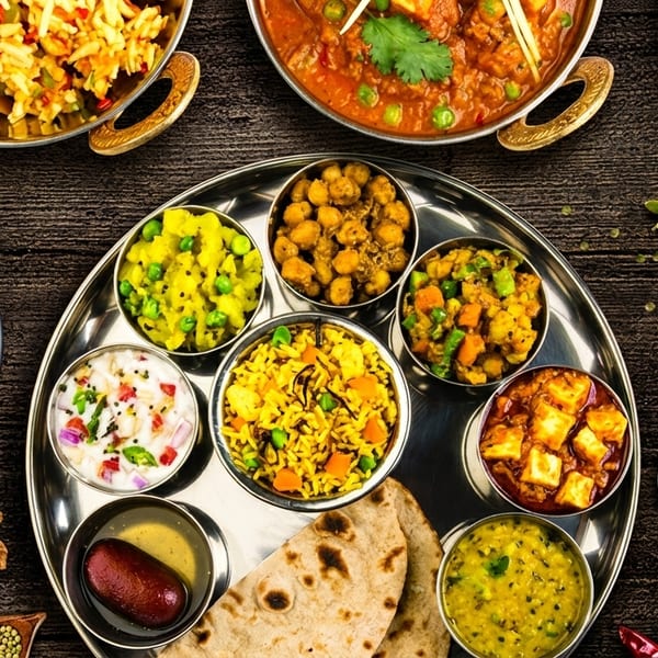 A vibrant Indian thali with various curries, rice, bread, and spices on a wooden table.