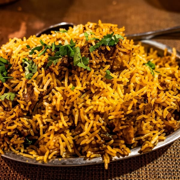 A large serving of chicken biryani, garnished with fresh cilantro, in a metal dish.