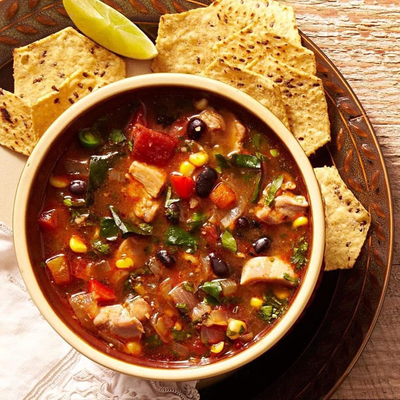 Hearty Indian chicken and vegetable soup with black beans, corn, and cilantro, served with lime and flatbread.