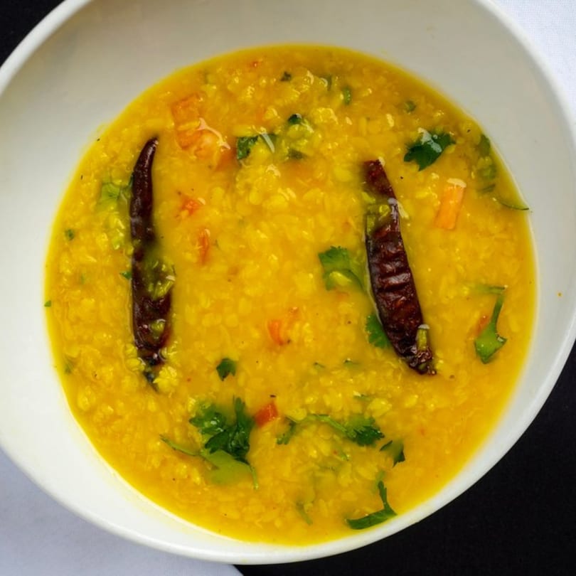 A bowl of vibrant yellow Indian dal, garnished with green herbs and two dried red chilies.