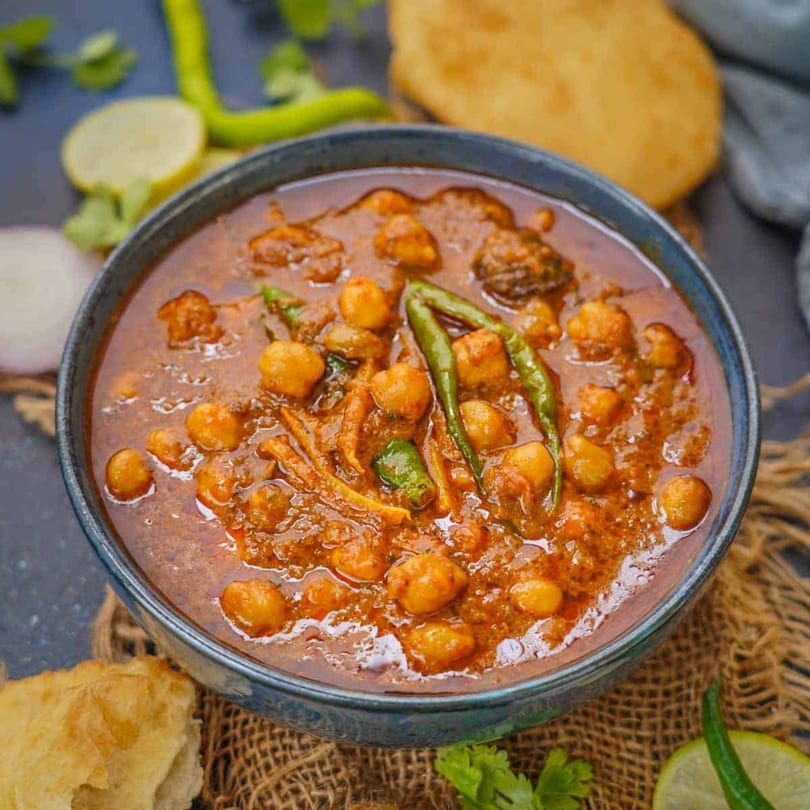 A bowl of Indian chana masala with green chilies, served with puri bread and lime.