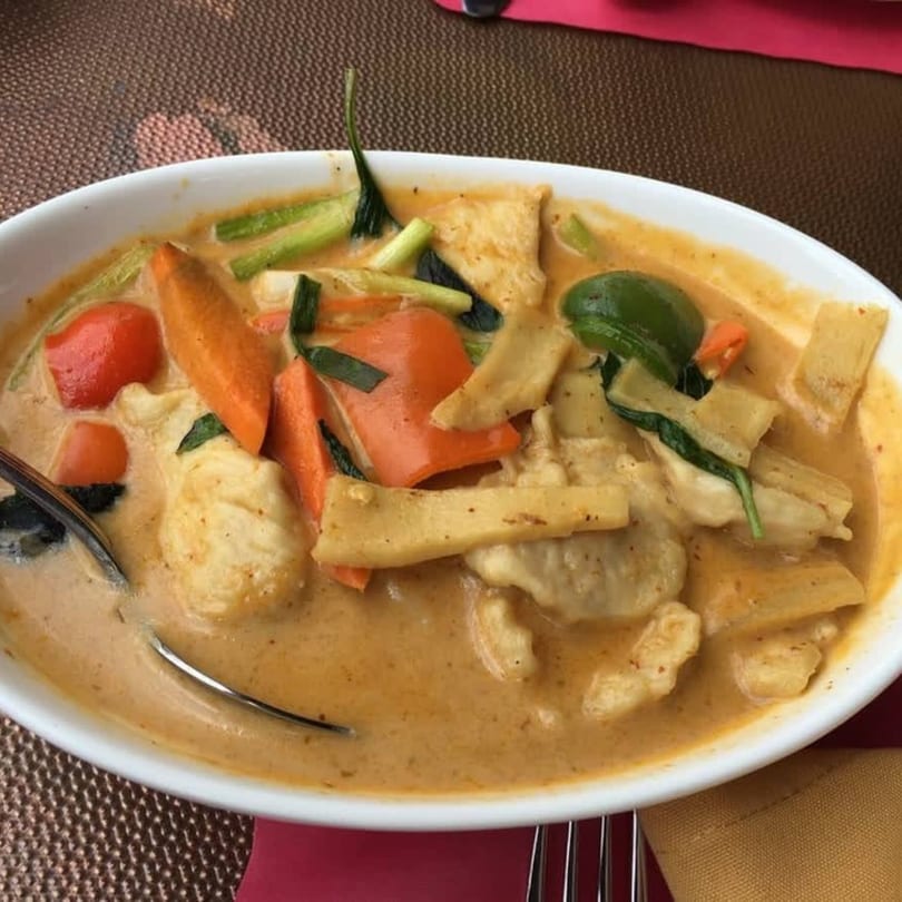 A white bowl of Indian curry with chicken, carrots, bell peppers, and bamboo shoots.