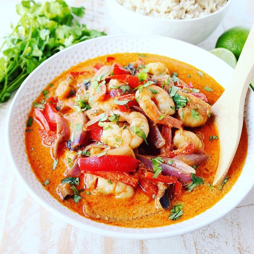 Indian shrimp curry with red peppers and onions, garnished with cilantro, served with rice and limes.