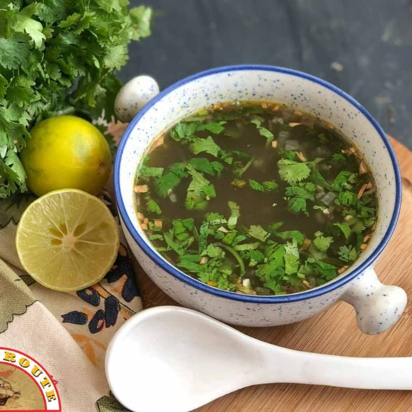 A bowl of Indian soup with cilantro, lime, and a white spoon on a wooden board.